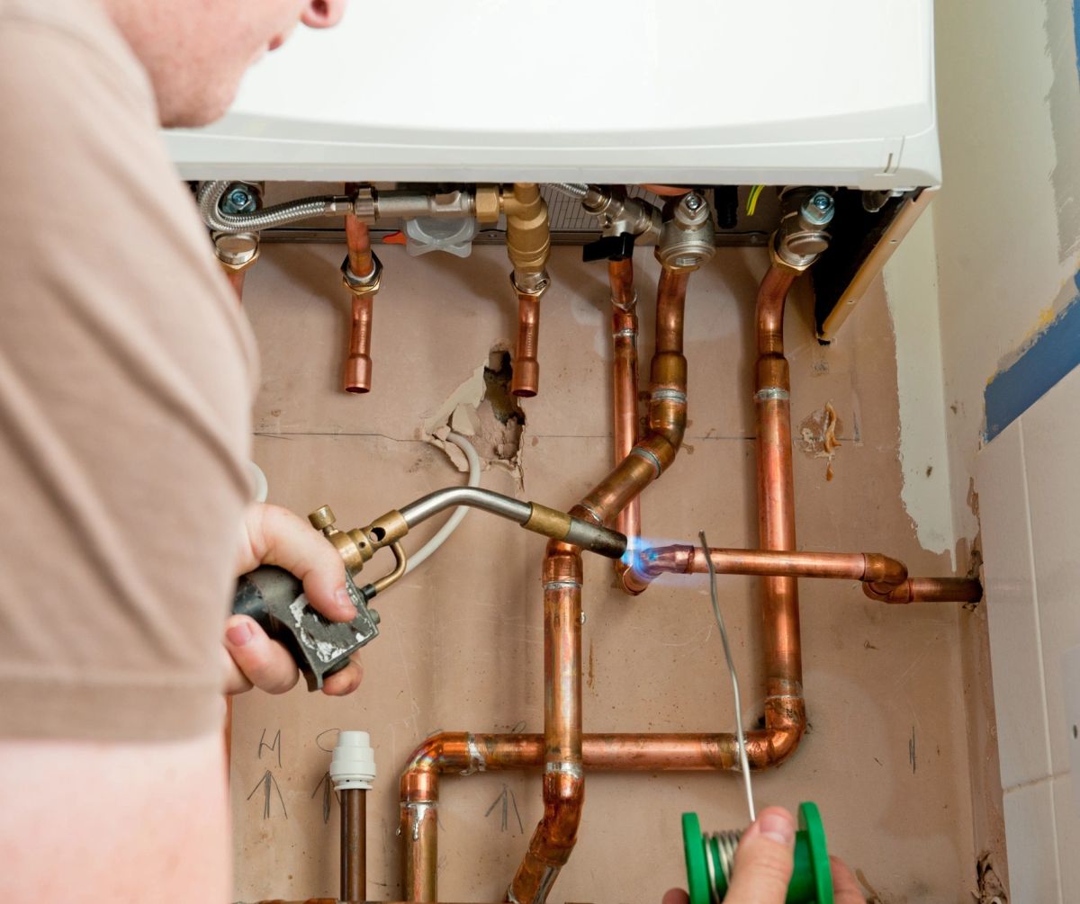 Engineer soldering copper pipework beneath a wall-hung boiler