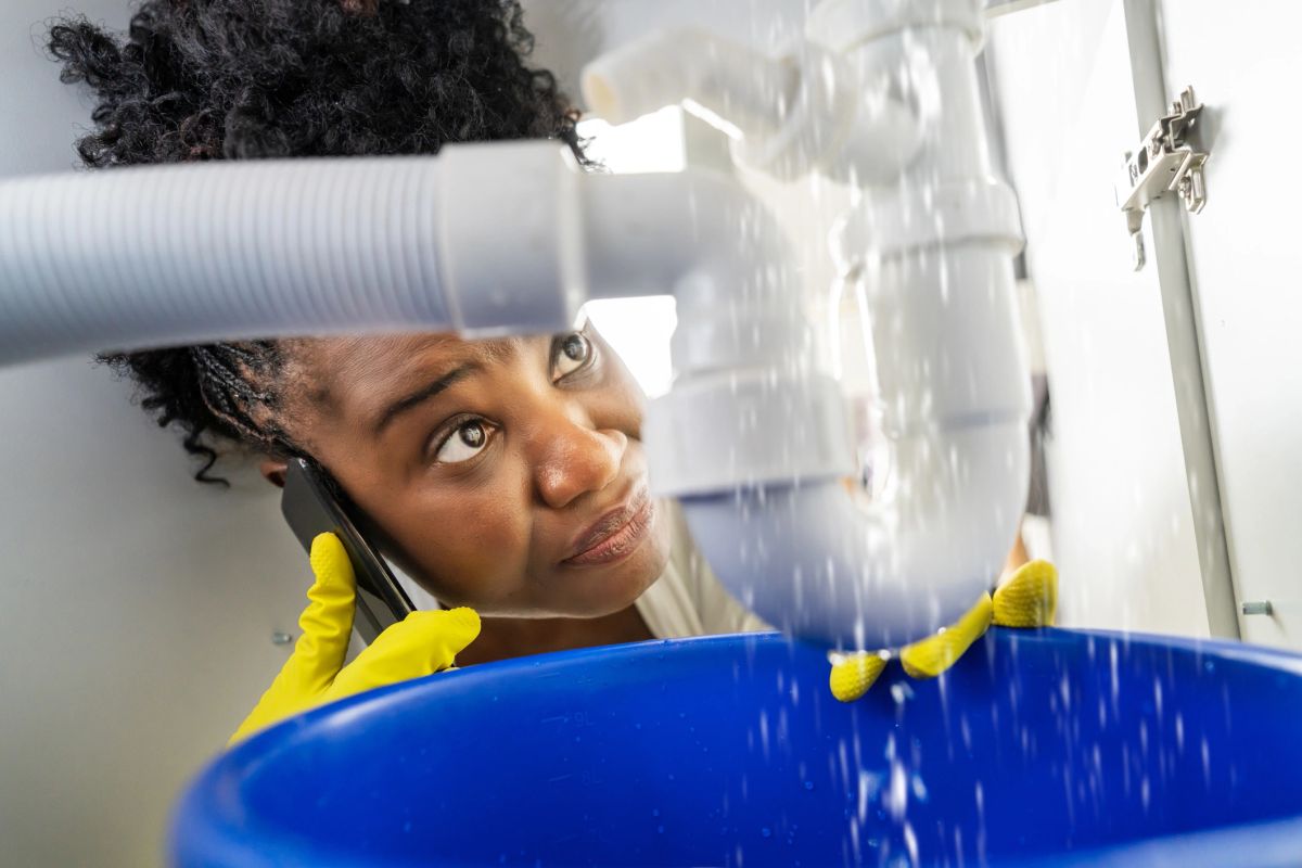 Person on the phone holding a bucket under a leaking waste pipe