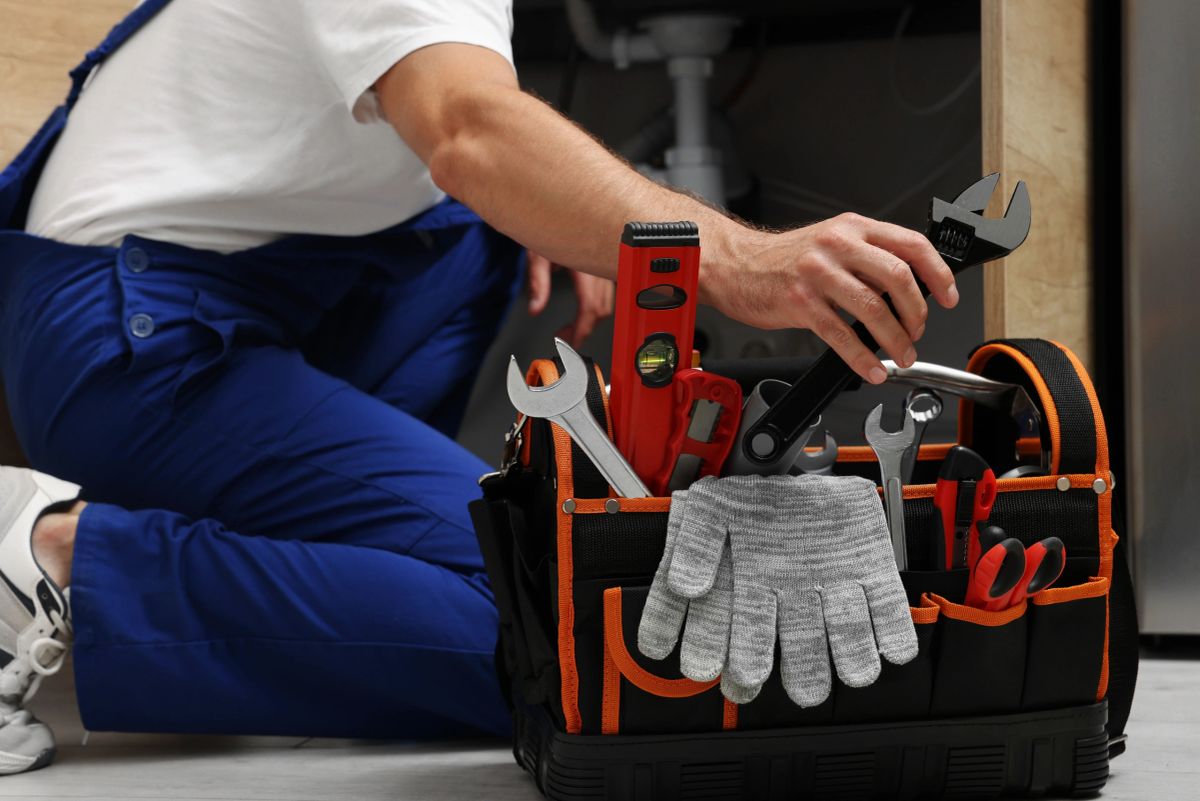 Engineer reaching into a tool bag under a sink